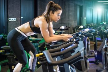 Attractive young woman in sportswear cycling in gym.